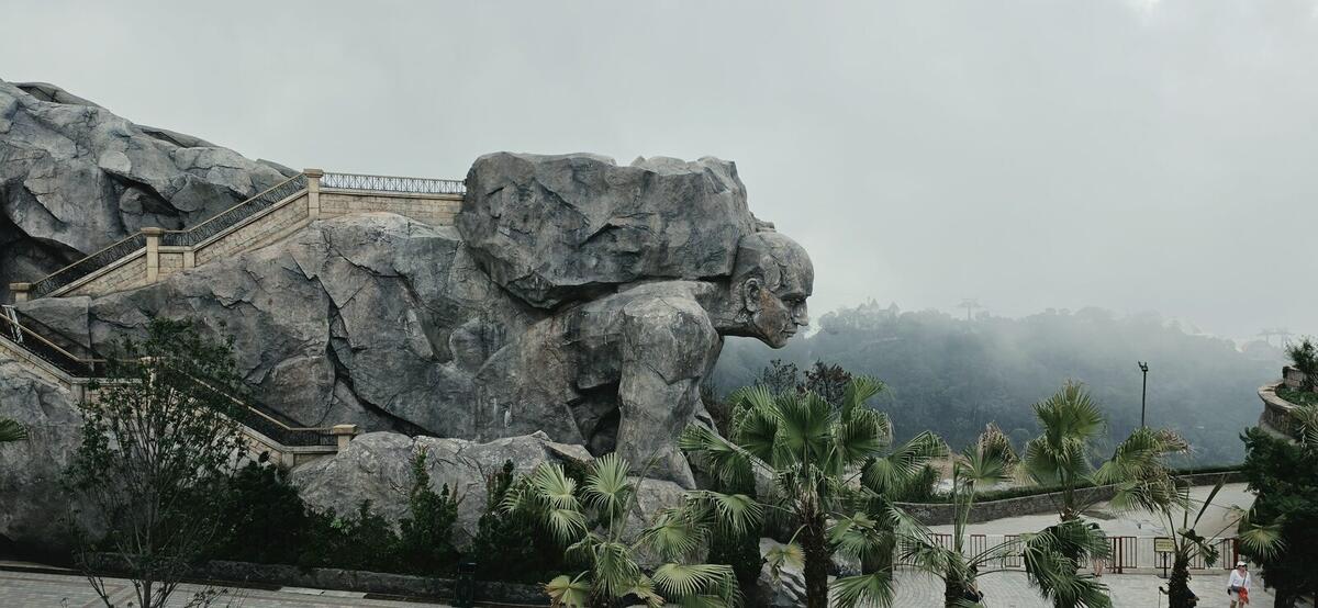 Giant stone figure sculpture emerging from the mountainside in fog