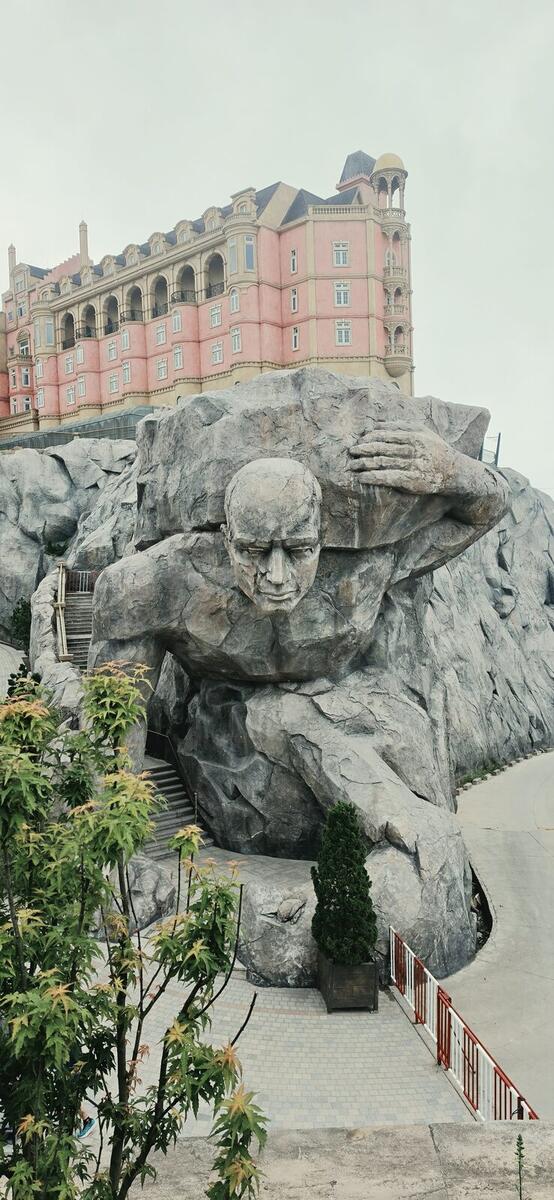 Giant stone figure sculpture with a pink hotel building behind it