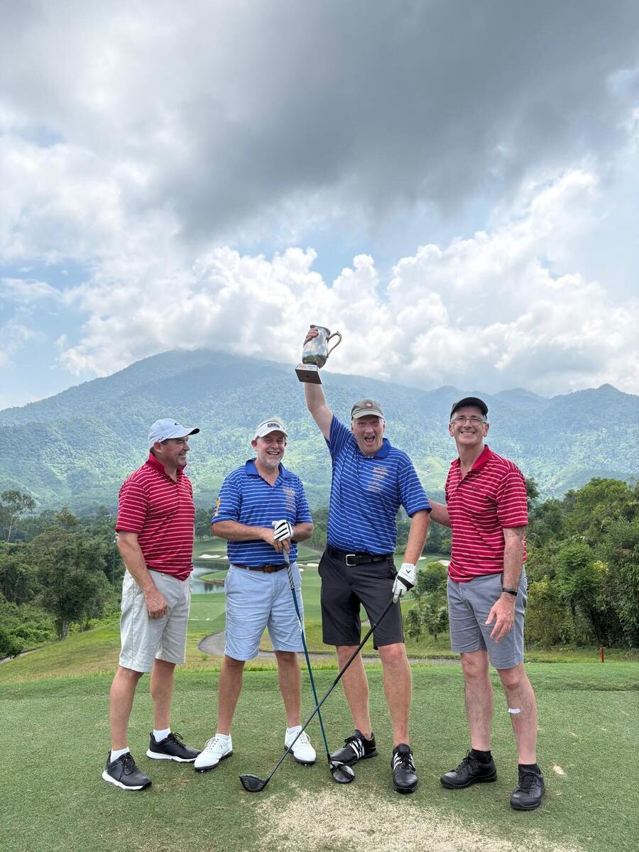 The crew holding the trophy aloft on the tee with the mountains behind