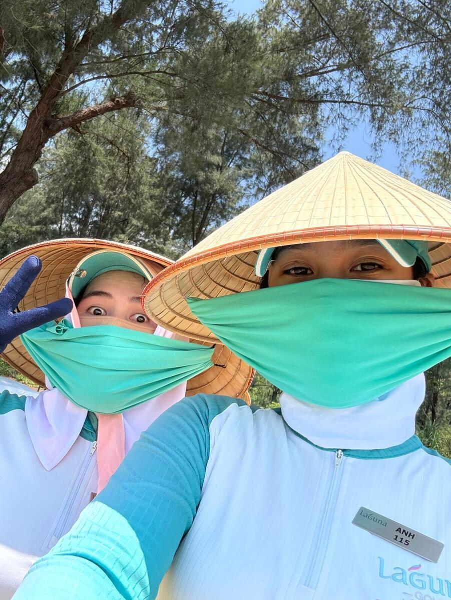 Two caddies in conical hats and face masks posing for a selfie