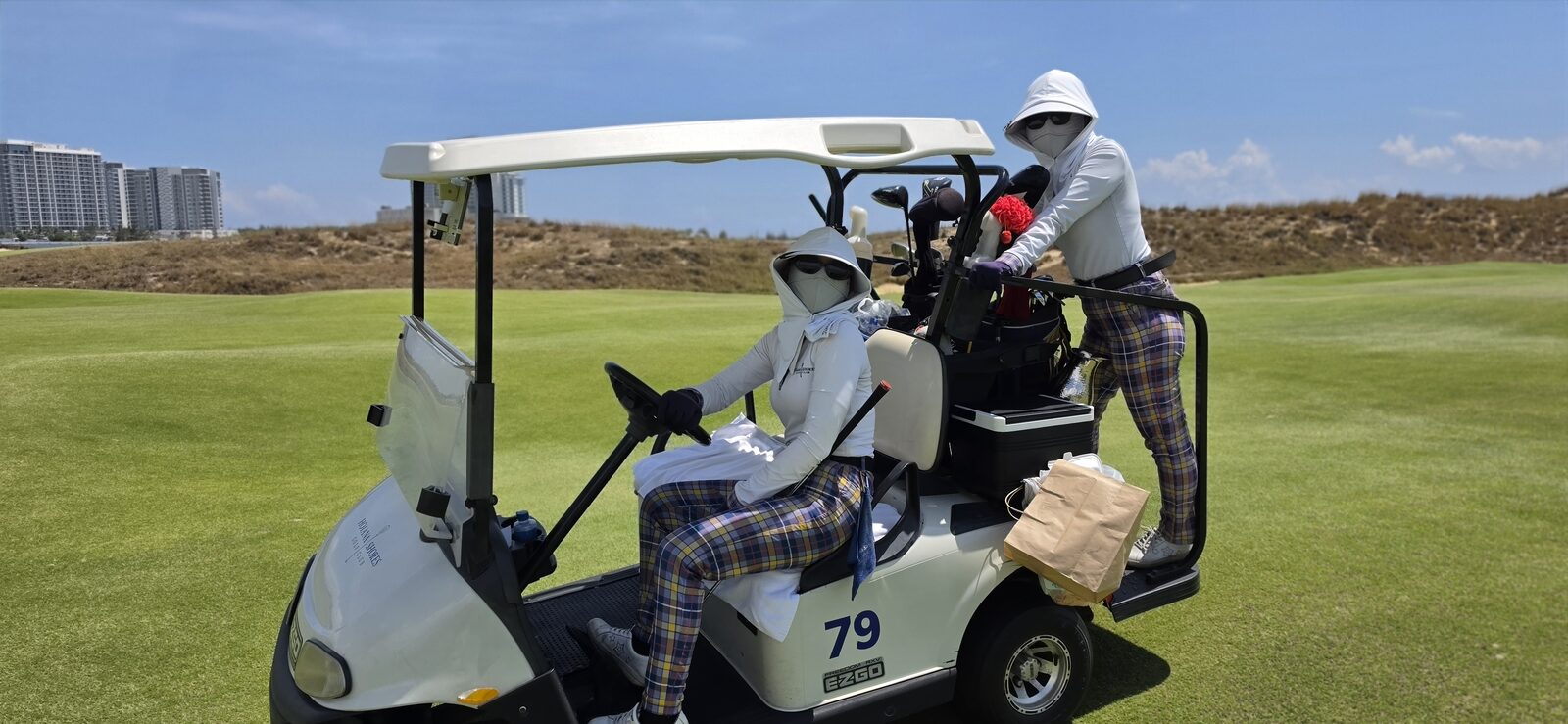 Two caddies covered up from the sun on a golf cart at Hoiana Shores